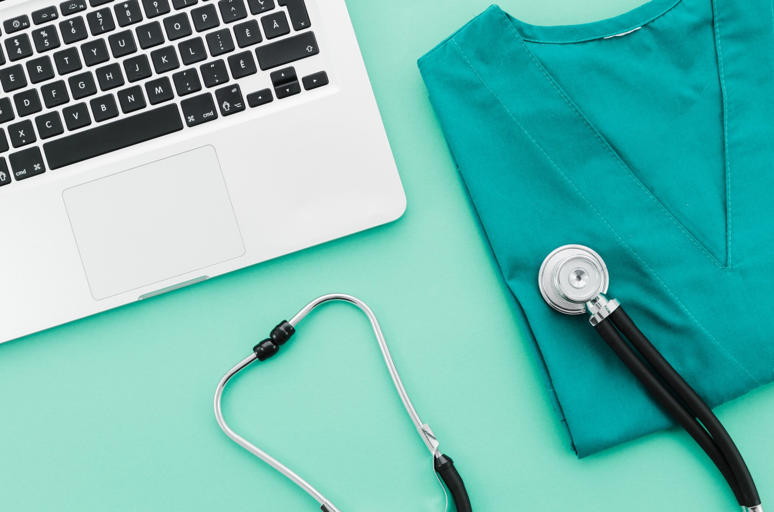 estetoscópio e uniforme médico em mesa ao lado de um notebook aberto