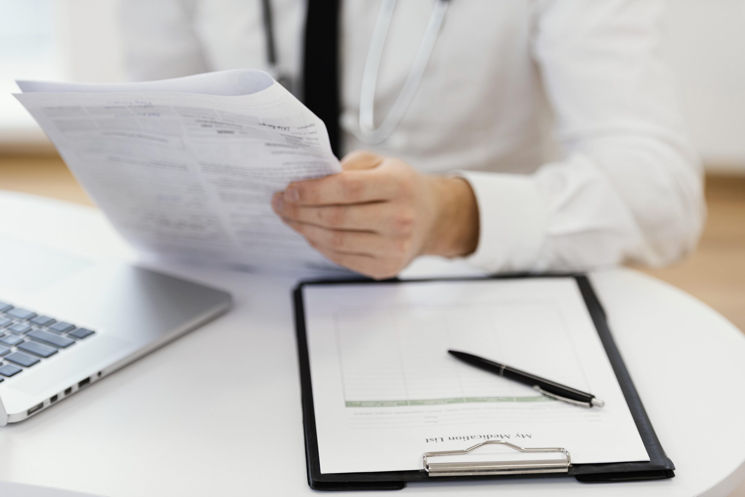 médico sentado na mesa analisando um papel e com uma prancheta ao lado